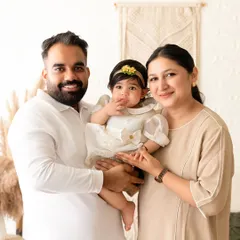A bright and happy family photo, with a mother, father, and baby smiling together in a boho-themed setting.
