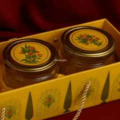 A classic and elegant Diwali gift. This set contains two glass jars with traditional floral-patterned lids, presented in a matching yellow gift bag, ready to be filled with festive treats.