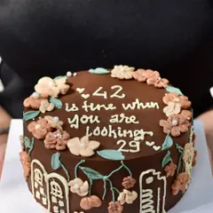 A custom chocolate birthday cake with a witty message, "42 is fine when you are looking 29." We love adding these personal touches, surrounded by hand-piped flowers and a Bombay-inspired skyline.