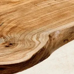 A close-up of a live-edge teak dining tabletop. The natural, uncut edge of the wood makes each table a unique statement piece, bringing organic beauty to your dining space.