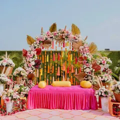 A beautiful Mehendi setup with a pink and gold theme, featuring a floral arch, traditional tassels, and elegant seating for the bride.