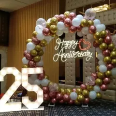 Celebrate a silver jubilee with a stunning photo corner. This 25th anniversary setup combines a circular balloon arch in rose gold, white, and chrome with large, illuminated marquee numbers to highlight your special milestone.