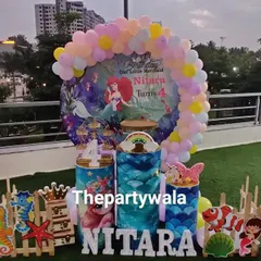 A beautiful outdoor Mermaid theme party on a rooftop. The setup includes a full backdrop, character cutouts, and themed props, creating an underwater wonderland with a city view.