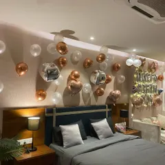A chic and modern birthday bedroom setup. The wall is decorated with a mix of rose gold, silver, and transparent balloons, including metallic orbs and heart shapes, creating a stylish backdrop above the bed.