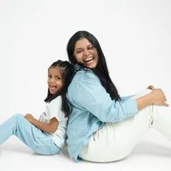 Leaning back-to-back, a mother and daughter share a laugh. This pose is fun and dynamic, showing their close and playful relationship.