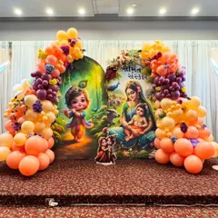 A vibrant Krishna-themed 'Simant Sanskar' ceremony with a custom backdrop in Gujarati script. The decor is brought to life with a colorful balloon arch in orange and purple.