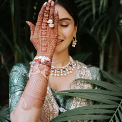 A playful and artistic shot for a Mehendi look. The makeup is minimal and glamorous, with softly accentuated eyes and glowing skin that looks beautiful against the lush green background.