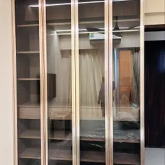 This elegant floor-to-ceiling wardrobe features tinted glass profile doors with a rich wood finish. The design offers a sophisticated way to display and organize your belongings, blending seamlessly into a modern bedroom aesthetic.