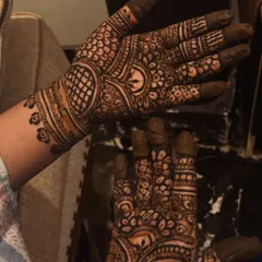 A close-up shot of the fresh henna paste on the palms. This design features a mix of netting, floral work, and paisleys, all applied with crisp, clean lines.