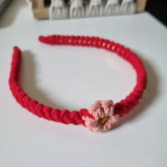 A single red macrame headband with a delicate pink flower. This piece is perfect for adding a pop of color and a touch of handmade charm to your hairstyle.