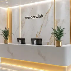 We designed this high-end reception area for "wonders.lab" to be impressive and professional. The space features a custom desk and a stunning floor-to-ceiling marble accent wall with gold-veining, complemented by warm under-desk lighting and elegant brass planters.