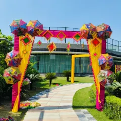 A daytime view of the colorful entrance arch decorated with Rajasthani umbrellas and bright pink and yellow drapes. This design is perfect for creating a fun and memorable entry point.