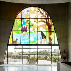 The view from inside the main entrance lobby, looking out through the 'Garden of Eden' stained glass window. The design allows natural light to filter through the coloured glass, creating an inspiring and contemplative atmosphere in the reception area.