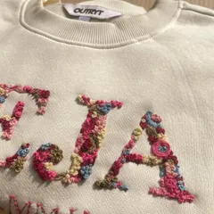 A close-up of the magic. I love filling initials with tiny, colorful flowers. Each petal and leaf is stitched by hand, making every floral letter a unique piece of art, like this 'TEJA' sweatshirt.