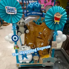 I love creating themed birthday hampers for kids. This one was for a first birthday, featuring a Shinchan and Snoopy theme with clothes, soft toys, and fun decorations, all in a bright blue setup.