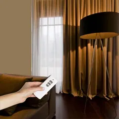 Setting the perfect mood is as simple as pressing a button. Here, a remote is used to adjust the rich, brown automated curtains in a cozy living room, showcasing the effortless elegance my systems provide.