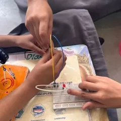 A close-up of students' hands as they carefully connect jumper wires to a breadboard, a fundamental skill in learning electronics and prototyping.