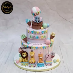 A playful two-tier jungle train cake for a second birthday. This choco-vanilla cake features an elephant in a hot air balloon and a train carrying a tiger, giraffe, and lion.