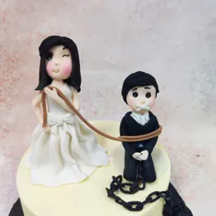 A close-up of the witty bride and groom toppers, showcasing the "ball and chain" detail with a heart lock.