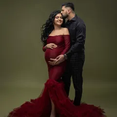 A tender moment in the studio. He gently kisses her forehead as she cradles her bump, both dressed in elegant, coordinating outfits.