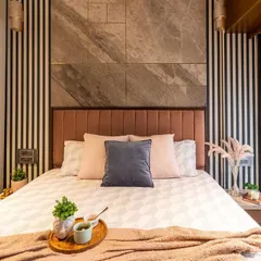 We love playing with textures to add depth. This bedroom features a dramatic backdrop of striped wallpaper and large-format marble-look tiles, balanced by a soft, dusty rose headboard.