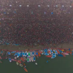 A top-down view of the riverbank at the Kumbh Mela. You can see the sharp line between the shore, packed with devotees, and the fleet of colorful boats waiting on the Ganga.
