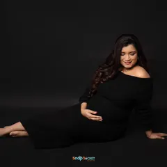 A simple, elegant portrait of the mom-to-be in a classic black off-the-shoulder dress. The dark backdrop and focused lighting create a moody and sophisticated feel.