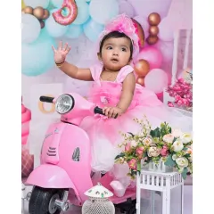 Waving hello from her pink scooter, this little girl is the star of her 'Candy Land' themed portrait. The pastel balloons and sweet treat props complete this vibrant setup.