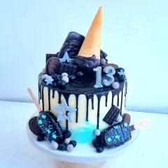 A fun drip cake for a 13th birthday. This design includes a dark chocolate drip, chocolate-dipped cakesicles, and various chocolate candies.