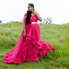 Standing tall in a field of green, this mom-to-be looks stunning in our vibrant pink ruffle gown. The dress features unique ruffles along the skirt and is cinched at the waist with a bold, embellished belt for a defined silhouette.
