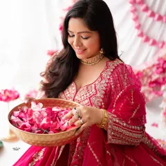 A beautiful portrait of a mother-to-be in a traditional pink outfit, holding a bowl of flower petals. The setup is rich with color and cultural aesthetics.
