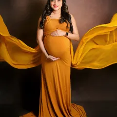 A classic maternity pose with a fabric toss for added movement and drama. The mom-to-be looks radiant in this mustard yellow gown against a simple, dark backdrop that makes the color pop.