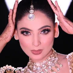 This shot highlights the neat bridal bun and the placement of the maang tikka. Notice how the model's hands with henna frame her face, adding to the traditional bridal aesthetic.
