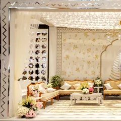 A side view of the elegant white and gold lounge. The space is defined by a mirrored frame with a zigzag pattern, soft drapes, and a mix of classic furniture and fresh floral arrangements.