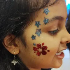 I love combining different elements to create a unique look. Here, I've paired a sparkling red flower on the cheek with a trail of blue glitter stars for a fun and whimsical face art design.