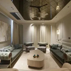 A full view of the South Ex living room, where custom olive green sofas add a pop of color to the neutral, monochromatic base. The space is tied together by a reflective ceiling, wainscoting on the walls, and carefully selected floral accent chairs.