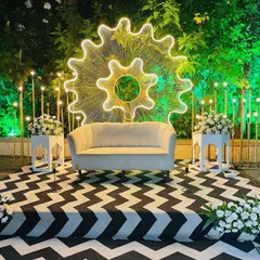 A modern and chic stage setup for a reception or cocktail night. The centerpiece is a large, illuminated gear-shaped backdrop on a black-and-white chevron floor.