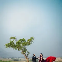 A wide-angle shot that shows the grand scale of the landscape for this pre-wedding shoot. The couple stands under a lone tree, creating a feeling of intimacy in a vast, open space.