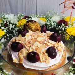 A close-up of the Cherry Almond cake within its floral hamper, showing the fresh cherries, toasted almonds, and a custom birthday topper.
