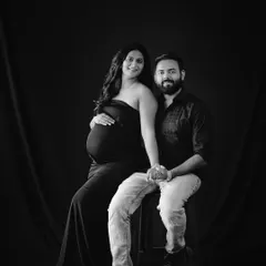 A beautiful seated portrait of a couple in black and white, holding hands and smiling for the camera. A timeless keepsake.