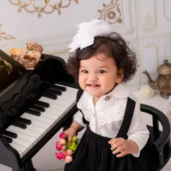 Flower in hand, music in soul. This little girl's bright, toothy smile is the star of this classic piano-themed portrait.