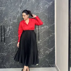 Power dressing with a feminine twist. A bold red shirt tucked into a black pleated midi skirt, paired with classic black pumps, creates a look that's perfect for the office or a formal event.