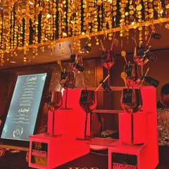 A stylish bar setup for a cocktail party, with red backlighting, custom drink stirrers, and a ceiling of hanging golden discs that shimmer and shine.
