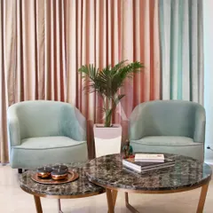 A close-up of the custom furniture in a pastel-themed living room. The nested coffee tables feature a beautiful marble top and brass legs, while the curved armchairs are upholstered in a soft mint green velvet.