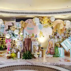 A wide shot of a charming Winnie the Pooh first birthday party. The decor features a soft, pastel color palette, a backdrop of the Hundred Acre Wood, and adorable cutouts of Pooh, Piglet, and their friends.