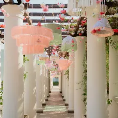 A whimsical entrance colonnade at a pastel Mehendi, with custom tassel chandeliers in shades of blush and pistachio hanging between grand white pillars, creating a dreamy pathway for guests.