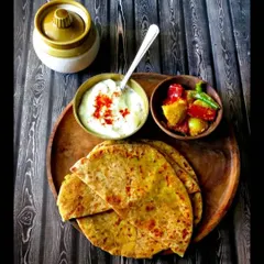 A beautifully plated shot of Stuffed Paratha with curd and pickle. This represents the breakfast offering and looks very appealing.