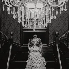 A beautiful black and white shot of the bride descending the stairs, framed by a crystal chandelier. This is an example of our artistic, cinematic approach to bridal portraits.