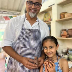 A father and daughter proudly holding the small clay figures they made together. These workshops are all about the shared experience of making something with your own hands.