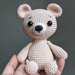 A classic, simple teddy bear in a lovely beige color, small enough to sit in the palm of your hand.